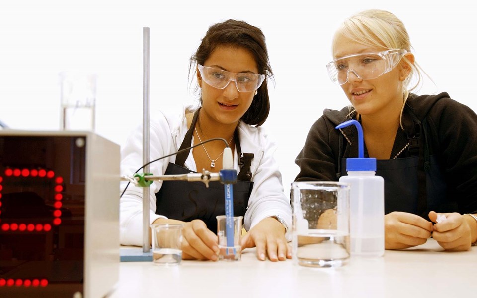 Två kvinnor med skyddsglasögon mäter något i ett lab 